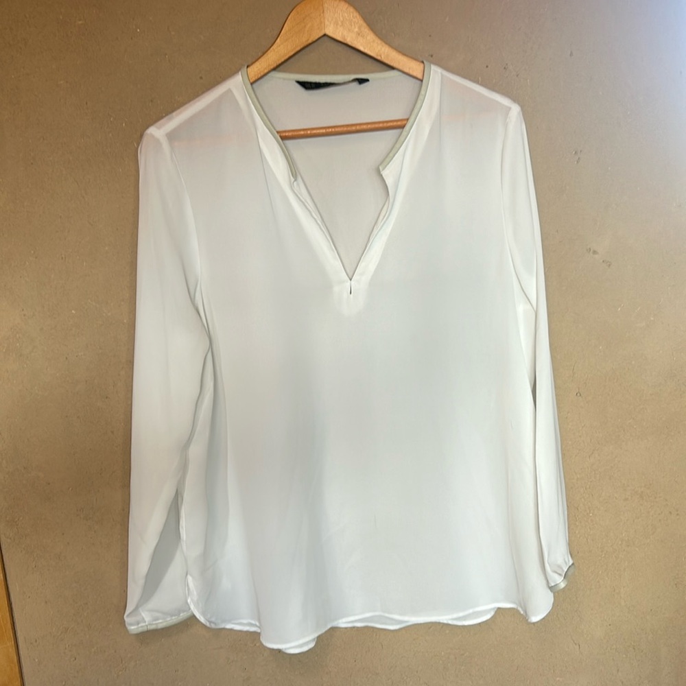 White polyester long sleeve top with faux leather trim at v-neck and cuffs.